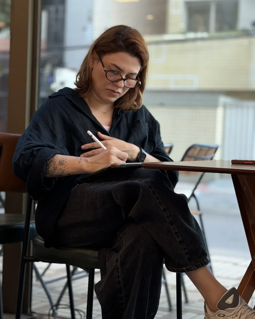 Cliente desenhando em um tablet sentada à mesa alta junto à vitrine do café