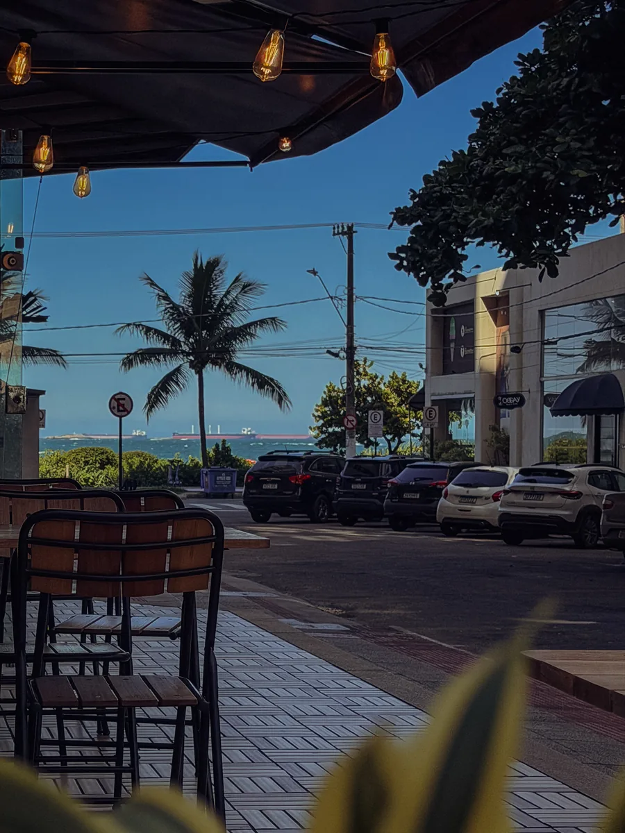 Vista da rua ao entardecer a partir de dentro do café, com palmeira e o mar ao fundo