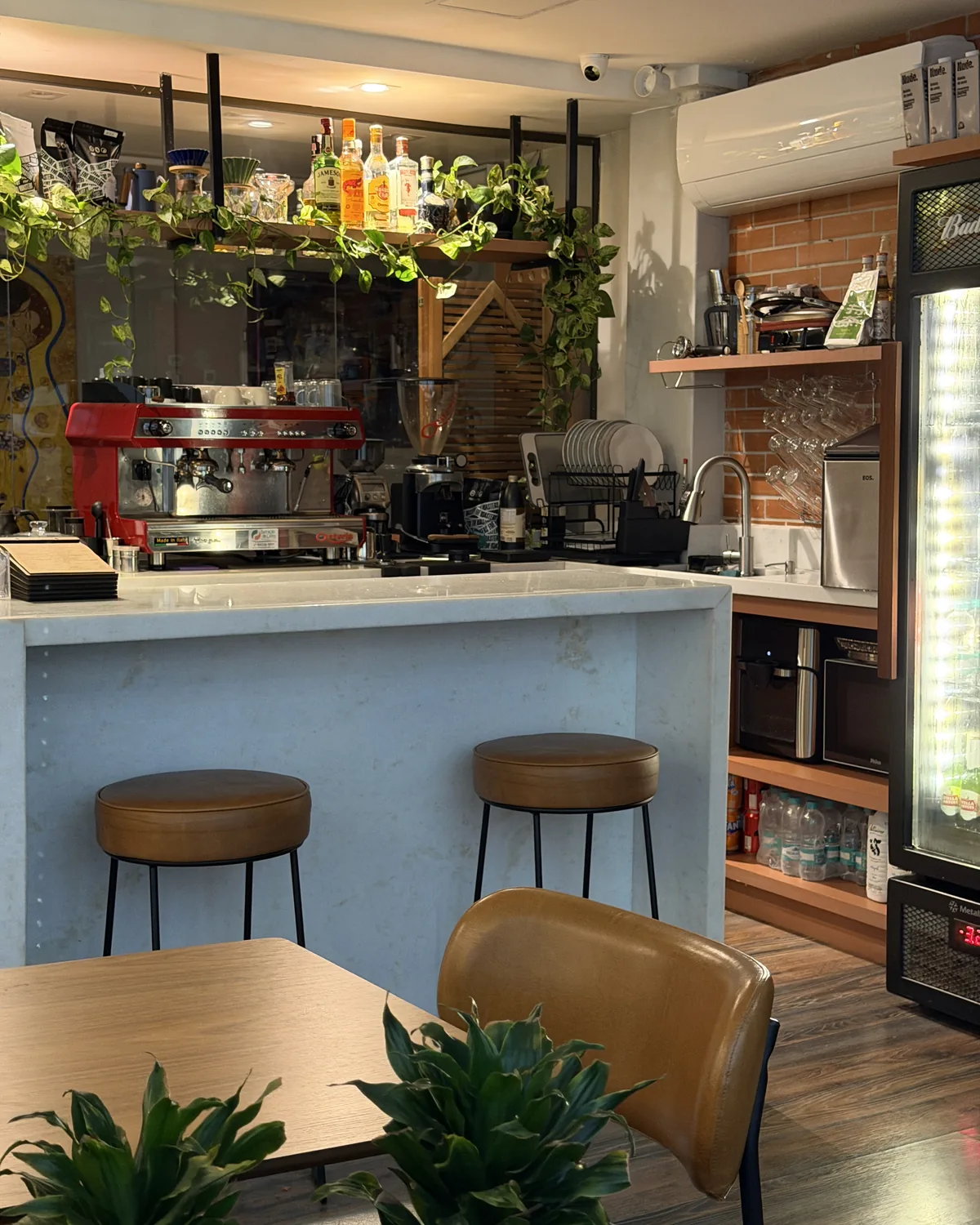 Balcão do Dois Britos com a máquina de espresso vermelha, bancada de mármore e banquetas